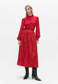 Red knitted sweater with long sleeves paired with a long floral-patterned red skirt. Black knee-high heeled boots complete the outfit.
