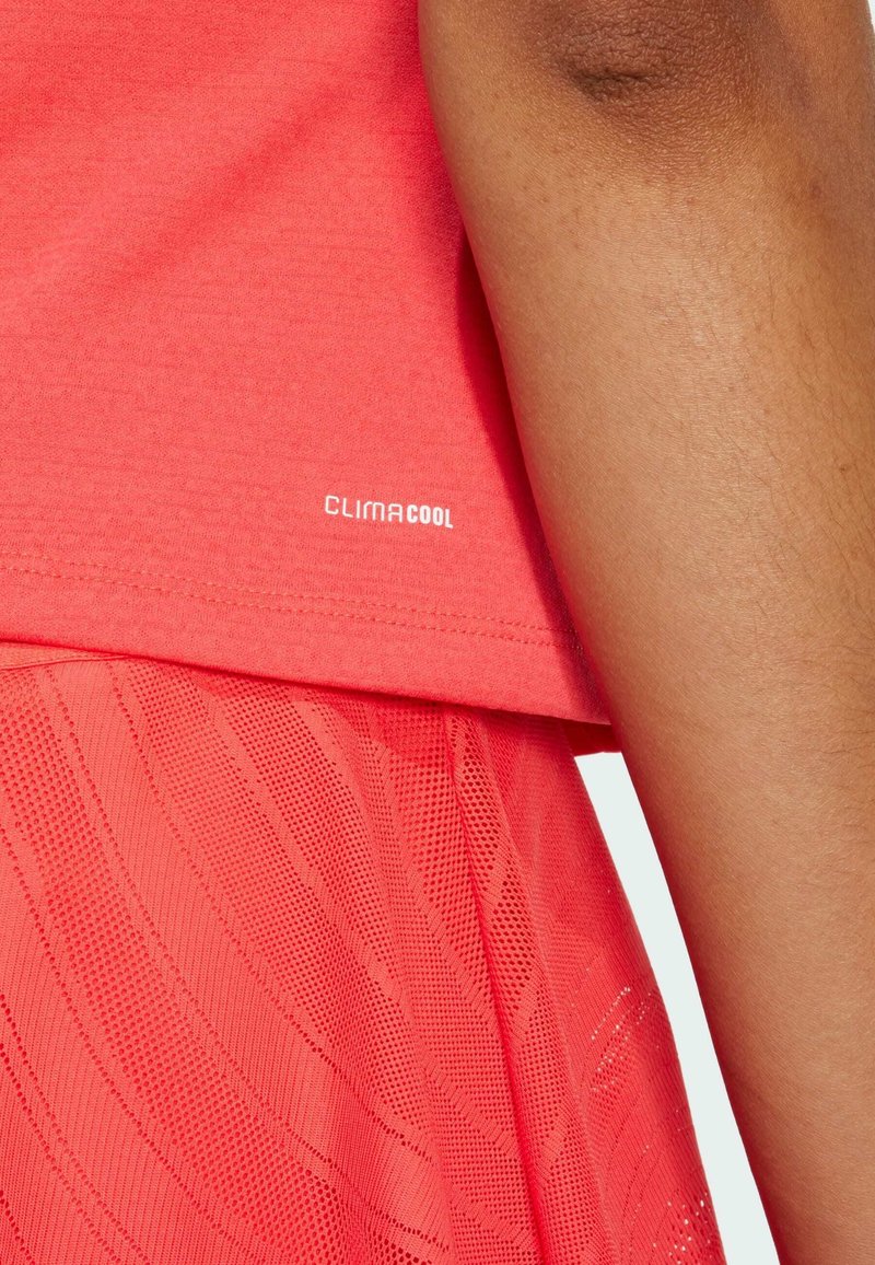 T-shirt de sport à manches courtes en corail avec un ourlet texturé ; présente le logo "CLIMACOOL", associé à une jupe en mesh superposée.