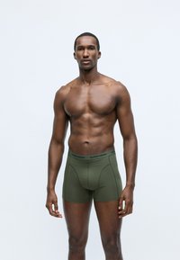 Boxer shorts verde oliva realizzati in tessuto morbido, con un design aderente e una cintura elastica che presenta la scritta "BJÖRN BORG" in nero.