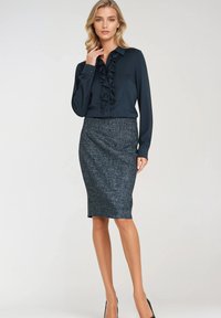 Niebieska bluzka z falbaniastym przodem, w połączeniu z teksturowaną spódnicą ołówkową w ciemnoszarym kolorze, podkreślona czarnymi szpilkami.