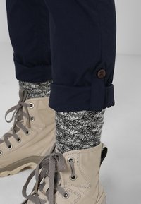 Námořnické kalhoty s manžetami na knoflíky, doplněné šedými pletenými ponožkami a béžovými šněrovacími botami. Vyznačují se texturovaným designem ponožek a pevnou materiálem bot.