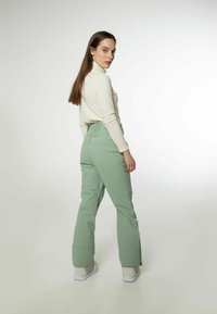 Grüne, lockere Hose mit hoher Taille, die einen Reißverschluss am Knöchel hat. Kombiniert mit einem langärmligen, cremefarbenen, gerippten Rollkragenpullover.