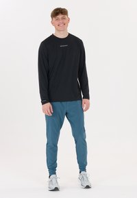 Svart långärmad atletisk tröja med vit text, kombinerad med teal tapered joggingbyxor. Grå sportskor fulländar outfiten.