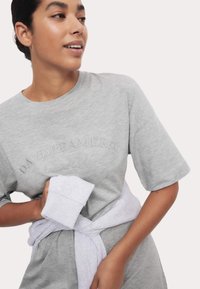 Grå oversized t-shirt i mjuk bomull med broderad text "DAYDREAMERS." En ljusgrå sweatshirt knuten runt midjan.