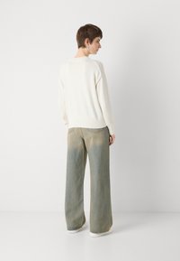 Hvit strikkegenser kombinert med vide, falmede blå jeans. Jeansene har en slitt tekstur med en subtil ombre-effekt mot bunnen.
