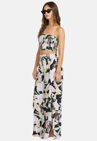 Completo a due pezzi composto da un top cropped senza spalline con stampa tropicale e pantaloni a vita alta con spacco in tonalità nere, verdi e rosa.
