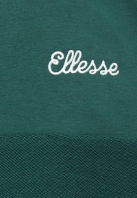 Tecido verde com o logótipo "Ellesse" em branco, bordado em estilo cursivo, centrado acima de uma costura texturizada.