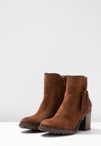 Brązowe zamszowe botki za kostkę z bocznym zamkiem, słupkowym obcasem i dekoracyjnym frędzlem z tyłu. Teksturowana podeszwa zapewniająca przyczepność i stabilność.