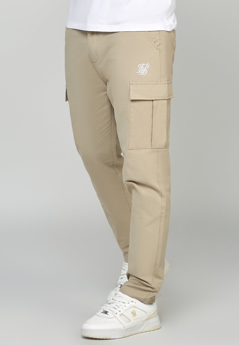 Beige cargobyxor med dragkedjefickor, elastisk midja och logotypdetalj. Tillverkade av ett slätt material, med en tapered passform och raka ben.