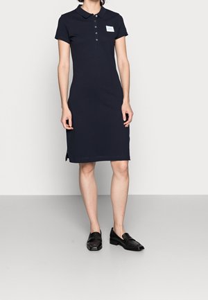 Navy sukienka polo z bawełny, z kołnierzykiem, plisą na guziki i bocznymi rozporkami, w połączeniu z czarnymi loafersami.