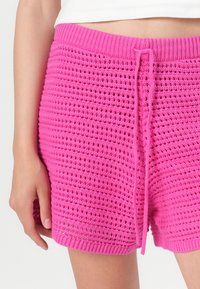 Pink knitted shorts with a textured pattern, drawstring waist, and ribbed hem. The fabric appears lightweight and breathable.
