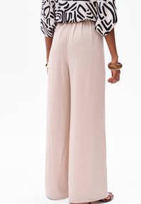 Lichte, beige wijde broek met een elastische tailleband. Vlotte textuur, vloeiende uitstraling. G gedragen met een gemêleerd zwart-wit top.