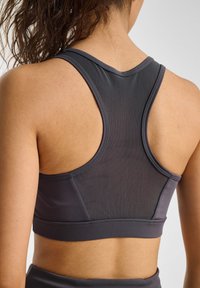 Donkergrijze sportbh van een gestructureerde, ademende stof. Heeft een racerbackontwerp en platte naden voor comfort en ondersteuning.