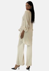 Romantisch crèmekleurig top met luchtige mouwen en een asymmetrische zoom, gecombineerd met wijde crèmekleurige broek en zwarte stilettohakken, met een gestructureerde stof.