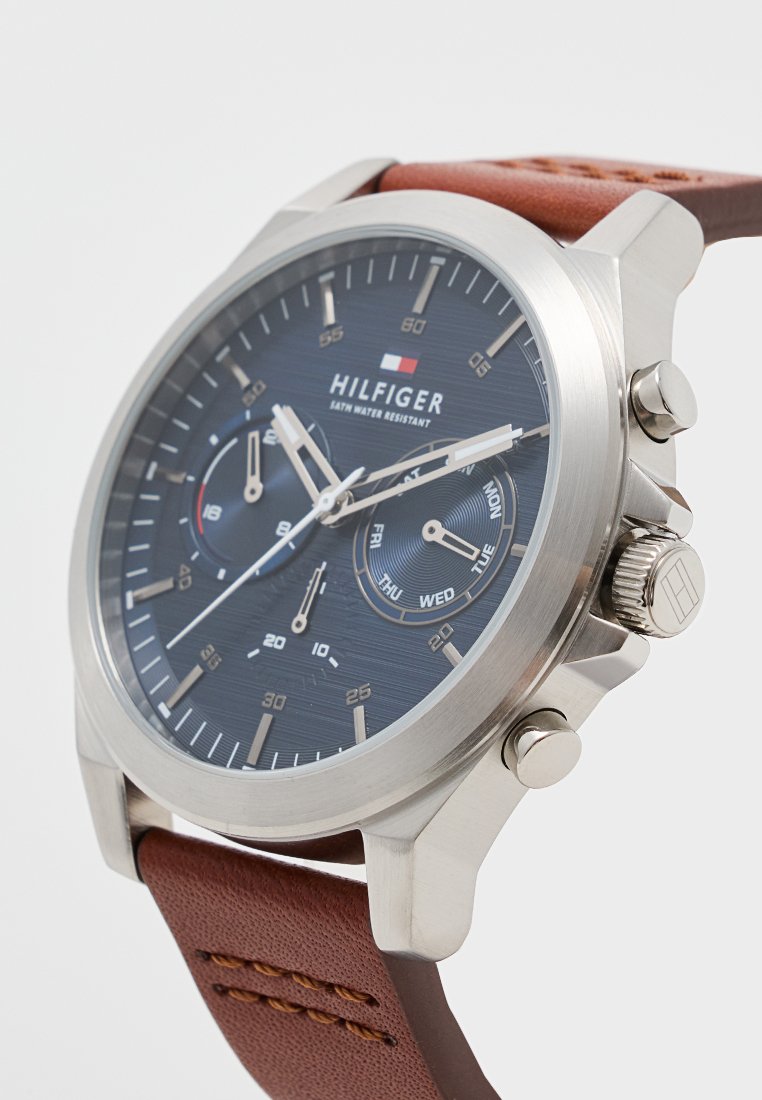 Reloj de acero inoxidable plateado con correa de cuero marrón. Esfera de color azul oscuro, con subdiales de cronógrafo, pantalla de fecha y marcadores luminiscentes.