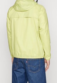 Jasnozielona kurtka z kapturem, z elastycznymi mankietami i dołem. Posiada kontrastowy tylny karczek. Połączona z ciemnoniebieskimi dżinsami. Gładka, lekko błyszcząca tekstura.
