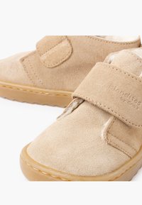 Zapatos de ante beige con un interior suave, que cuentan con una amplia tira de Velcro y una suela de goma texturizada. Diseño compacto con punta redondeada.