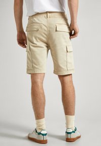 Pantalones cortos cargo beige con múltiples bolsillos, bordes dobladillos y un ajuste relajado. Combinados con zapatillas blancas y calcetines de canalé color crema.