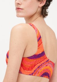 Ένα πολύχρωμο μπικίνι σουτιέν που διαθέτει σ swirling σχέδια σε αποχρώσεις πορτοκαλί, ροζ και μωβ. Ευρείς ιμάντες και υφή υφάσματος.