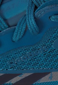 Primer plano de una zapatilla Reebok azul mostrando los cordones texturizados, la tela de malla y el logotipo de la marca en el panel lateral y en la lengua.