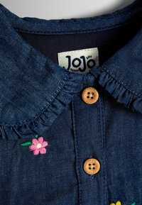 Tumesinist teksasärk volangidega krae, puidust nööbi sulgemine ja roosa-rohelise kirju lillemustriga tikanddetail. JoJo brändi silt nähtaval.