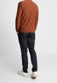 Brun stickad tröja med ribbade fållar, tillsammans med svarta randiga byxor och vita låga sneakers, sedd bakifrån.