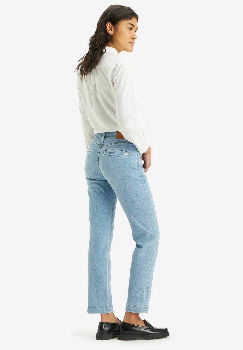 Helle blaue, gerade geschnittene Jeans aus Denim mit einer mittelhohen Taille, zwei Gesäßtaschen und einer strukturierten Oberfläche. Kombiniert mit einem weißen Hemd.