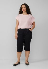 T-shirt rose clair à manches courtes associé à un pantalon noir coupé. Le pantalon possède un ourlet roulé et des poches latérales. Porté avec des ballerines noires.