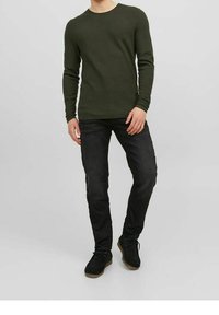 Zielona oliwkowa koszula z długim rękawem i okrągłym dekoltem, połączona z ciemnymi dżinsami i czarnymi butami, tworząca swobodny strój.