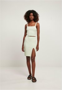 Conjunto de dos piezas de punto acanalado en verde claro que incluye un top corto de escote cuadrado y una falda hasta la rodilla con una abertura lateral. Sandalias negras completan el look.