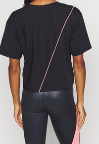 Svart kortärmad skjorta med ett strukturerat meshdesign, har en diagonalt rosa accentlinje över ryggen, kombinerad med åtsittande blanka leggings.