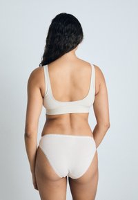 Beige sports-bh og matchende hipster truser med en glatt tekstur, brede stropper og lavt utskåret bak. Enkel design med subtil søm.