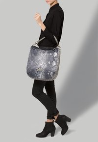 Grå och svart faux ormskinn axelväska med rundad form, mönstrad textur och metallaccessoarer. Bärhandtag är fäst.