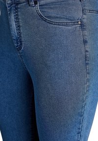 Vaqueros de mezclilla azul oscuro con un diseño ajustado, sutiles desgastes y un estilo clásico de cinco bolsillos con remaches metálicos. Textura suave.