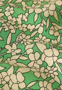 Tessuto verde con un motivo floreale in bianco sporco e nero. Il design include vari fiori e foglie con una superficie texturizzata.