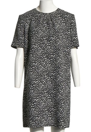 Robe droite à manches courtes noire et blanche avec un motif de points irréguliers sur un buste et des bras de mannequin blanc.