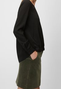 Schwarzes Langarmshirt mit rundem Ausschnitt, strukturiertem Stoff und gerafftem Saum, kombiniert mit einem olivgrünen Rock mit Taschen.