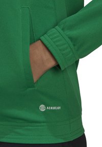 Grön Aeroready-jacka med texturerat tyg, instuckna fickor och elastiska ärmslut. Logotypen visas på nedre framsidan i vitt.