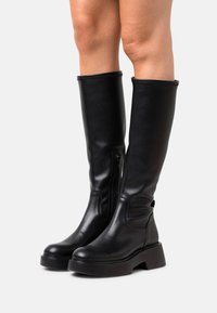Botas de cuero negro hasta la rodilla con punta redondeada, tacón robusto, cremallera lateral y acabado texturizado. Parte superior lisa con acentos mínimos.