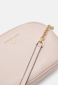 Bolso cruzado de cuero rosa con una superficie texturizada, herrajes dorados y un acento de cadena. Presenta un logotipo embossado en la parte frontal.