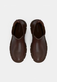 Een paar donkerbruine leren instap schoenen met dikke, geprofileerde zolen en aantrek-uitsparingen aan de hiel, gemarkeerd met "ANNA FIELD" aan de binnenkant.