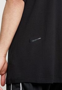 Svart Nike t-shirt med strukturerad tyg, korta ärmar och en liten svart broderad logotyp på vänster sida nära fållen.