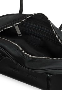 Interno di una borsa in pelle nera con una tasca con zip e un'etichetta con il logo. Texture liscia, zip argentata e fodera in tessuto senza dettagli esterni visibili.