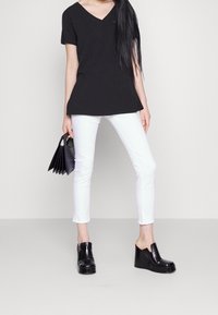 Černé tričko s výstřihem do V a krátkým rukávem, v kombinaci s bílými úzkými džíny. Modelka drží černou skladanou kabelku a má na sobě černé boty na platformě.