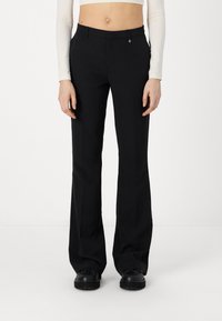 Pantalons évasés noirs en tissu lisse, dotés d'une fermeture éclair, de poches avant et d'un subtil accent métallique au-dessus de la taille.