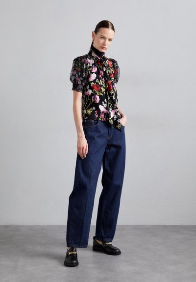 Floral patterned black blouse with puff sleeves, tied neck detail; worn with loose dark blue denim pants and black shoes with gold accents.