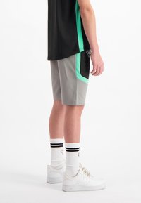 Grijze sportshorts met zwarte accenten en teal bies, gecombineerd met een zwart shirt. Witte sneakers en gestreepte witte sokken zijn zichtbaar.