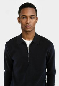 Maglione zip-up navy con collo, realizzato in tessuto morbido, dotato di chiusura a metà zip e maniche lunghe. Texture liscia, design minimalista.