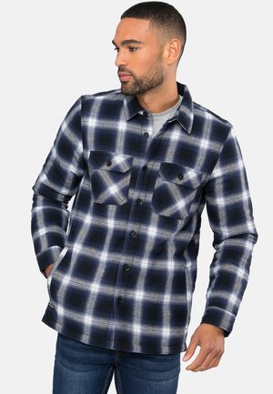 Marineblauw en witte geruite shirt met twee borstzakken, knoopsluiting aan de voorkant en een kraag. Gemaakt van zachte stof met een gestructureerd ruitpatroon.