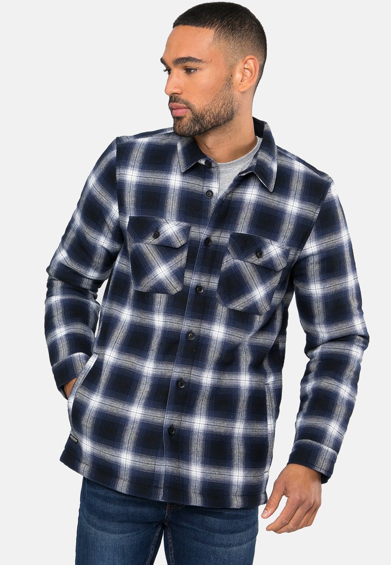 Marineblauw en witte geruite shirt met twee borstzakken, knoopsluiting aan de voorkant en een kraag. Gemaakt van zachte stof met een gestructureerd ruitpatroon.